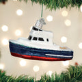 A Christmas tree ornament shaped like a small boat with white, blue, and red colors hangs among green tree branches, with blurred white lights in the background.