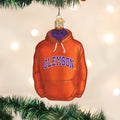 An ornament shaped like an orange hoodie with Clemson written across the front hangs on a Christmas tree with blurred white lights in the background.