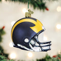 A Christmas tree ornament shaped like a football helmet with a navy blue and yellow design, hanging on a tree with blurred lights in the background.
