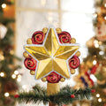 A shiny gold star tree topper with red spiral accents sits on top of a Christmas tree branch, with blurred festive decorations and lights in the background.