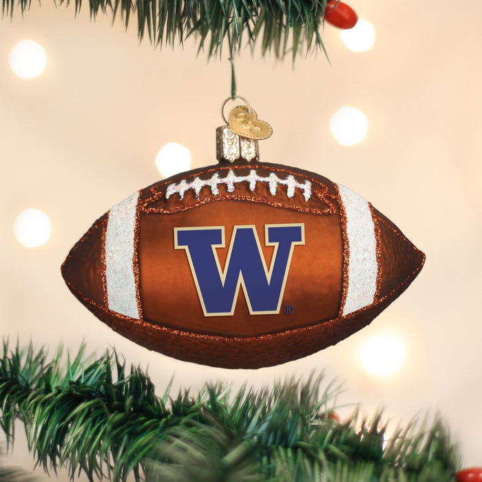A football-shaped ornament with a large purple W logo hangs on a Christmas tree branch, with blurred white lights in the background.