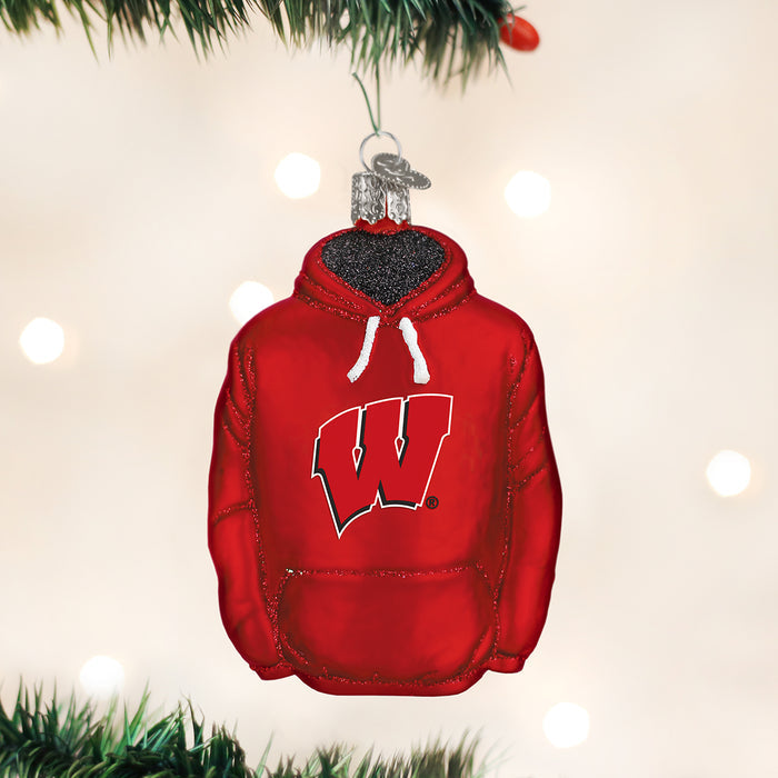 A Christmas tree ornament shaped like a red hoodie with a white W logo on the front, hanging from a branch with soft, blurred lights in the background.