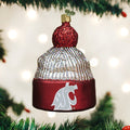 A Christmas tree ornament shaped like a red and silver knit hat, featuring the Washington State University cougar logo, hangs among green tree branches with blurred white lights in the background.